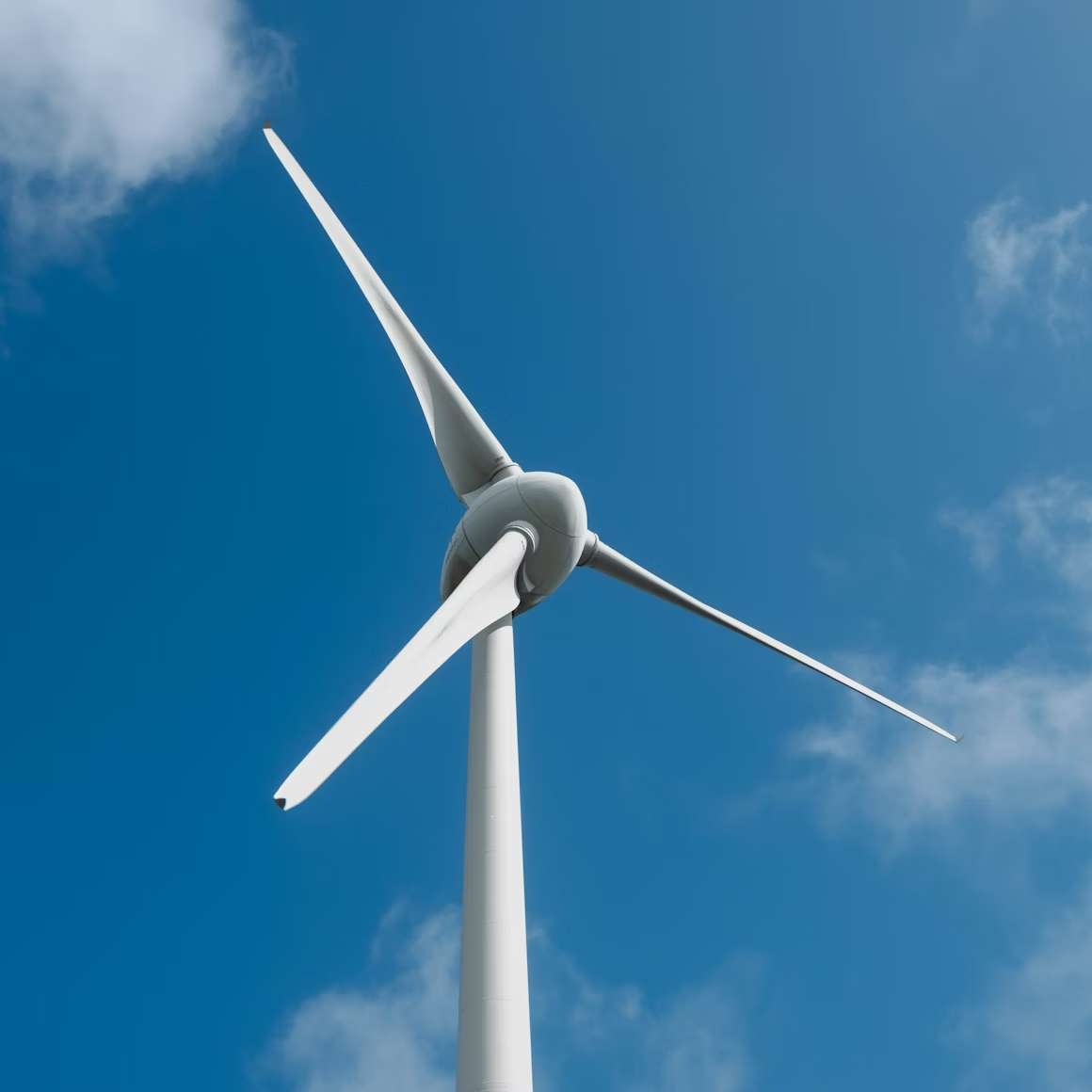 Close-up of a white wind turbine with three blades against a blue sky with scattered clouds.